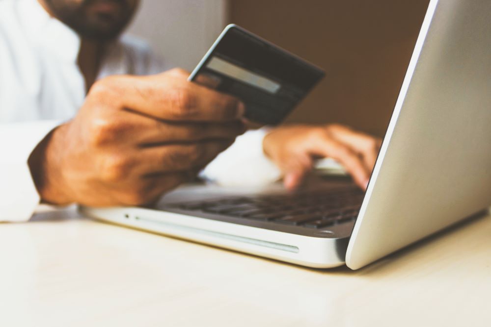 Man holding credit card sitting in front of laptop.